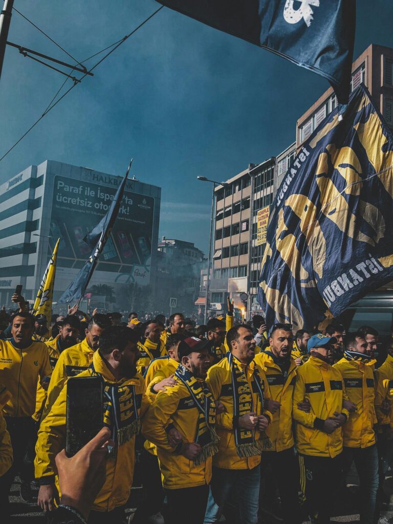 A crowd of Fenerbahce fans gather in Istanbul, waving flags and wearing team colors during a vibrant street celebration.
