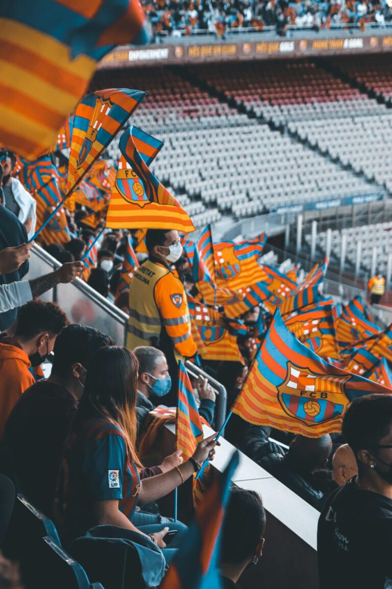 Excited football fans wave flags in a packed stadium, creating a lively atmosphere.